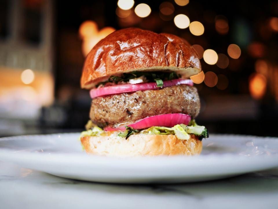 A burger on a brioche bun with red onion and lettuce