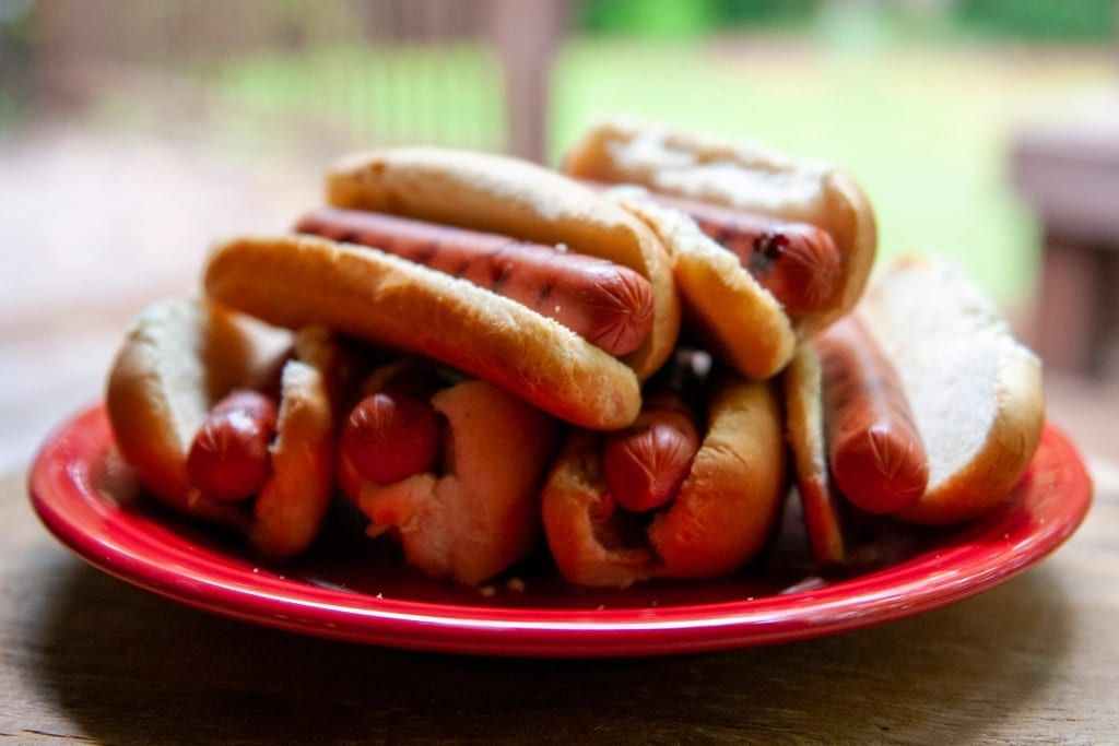 Grilled hot dogs in buns piled on a red plate