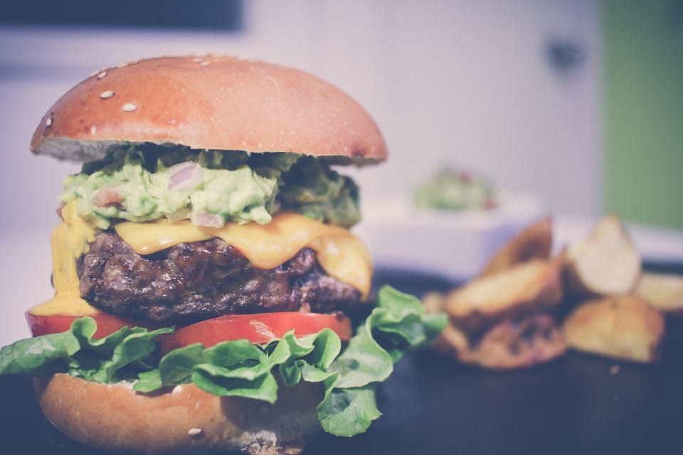 A cheeseburger topped with guacamole and tomato